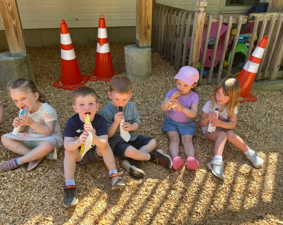 a group of kids sitting on the ground eating ice cream cones