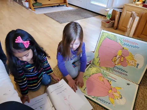 a couple of girls sitting on the floor looking at a book