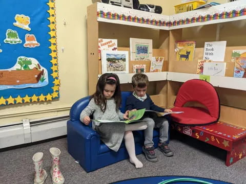 a couple of kids sitting on a blue chair in a room with a shelf with books and a