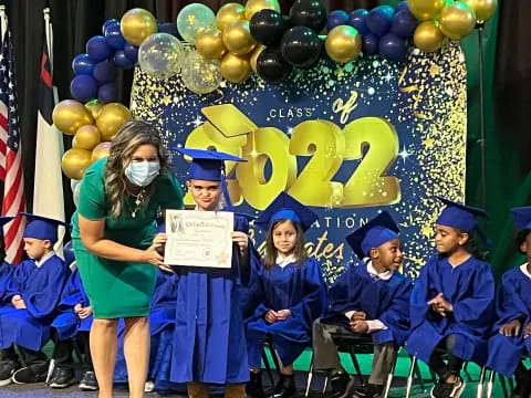a person standing in front of a group of children in graduation gowns