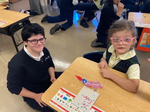 a couple of children sitting at a table with books and drawings