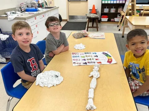 a group of boys sitting at a table with a paper airplane on it