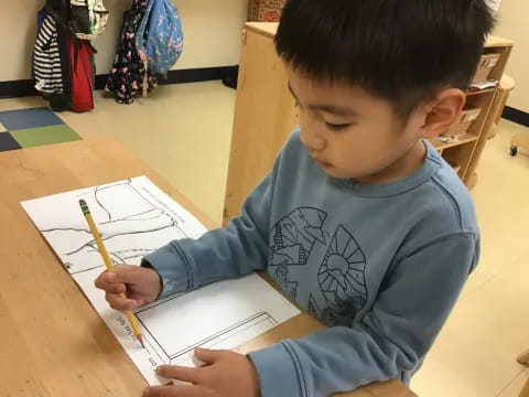 a young boy sitting at a table writing on a piece of paper