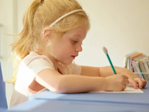 a young girl writing on a blue table