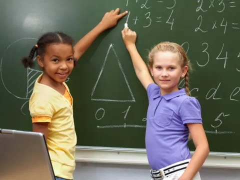 a couple of young girls writing on a chalkboard