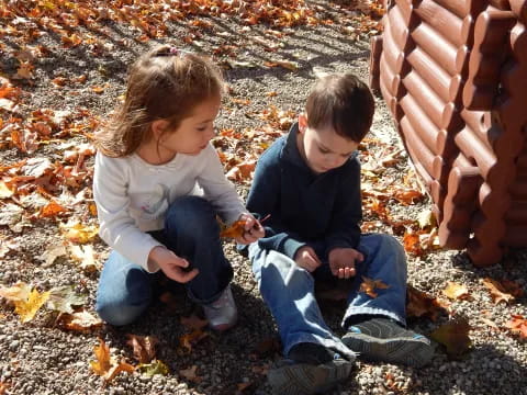 a boy and girl sitting on the ground looking at a cell phone
