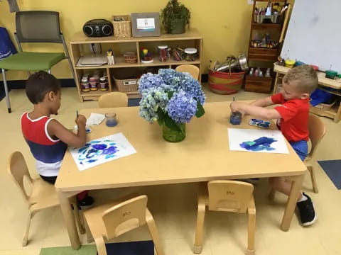 a couple of boys sitting at a table with a book and flowers