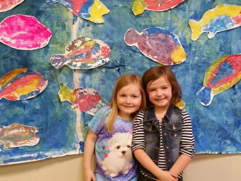 a couple of girls posing for the camera in front of a wall with art