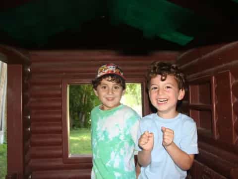 a couple of boys posing for the camera in front of a log cabin