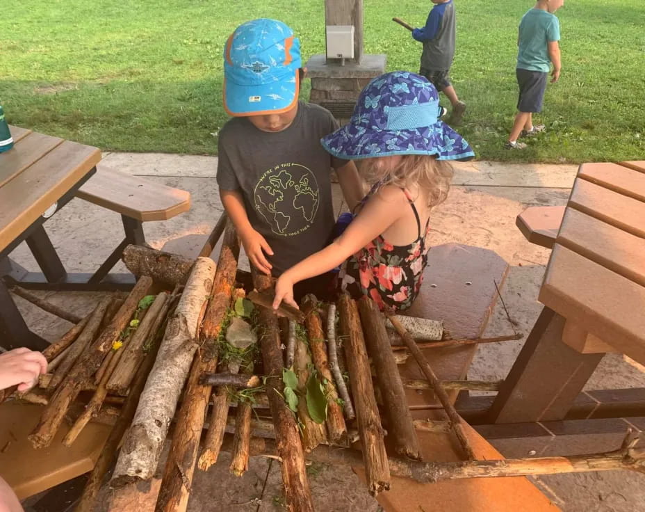 a couple of kids playing with a pile of leaves on a picnic table