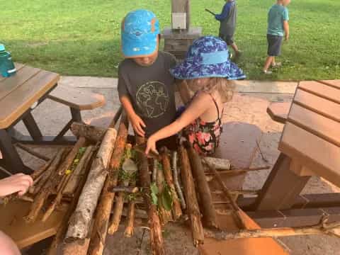 a couple of kids playing with a pile of leaves on a picnic table