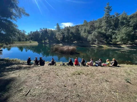 a group of people sitting on a rocky shore by a lake