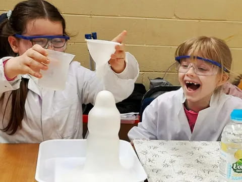 a couple of girls wearing safety goggles and holding up white plastic cups