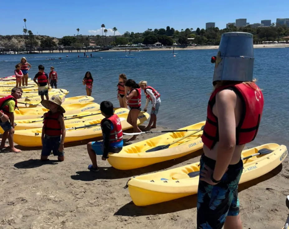 a group of people standing next to yellow kayaks on a beach