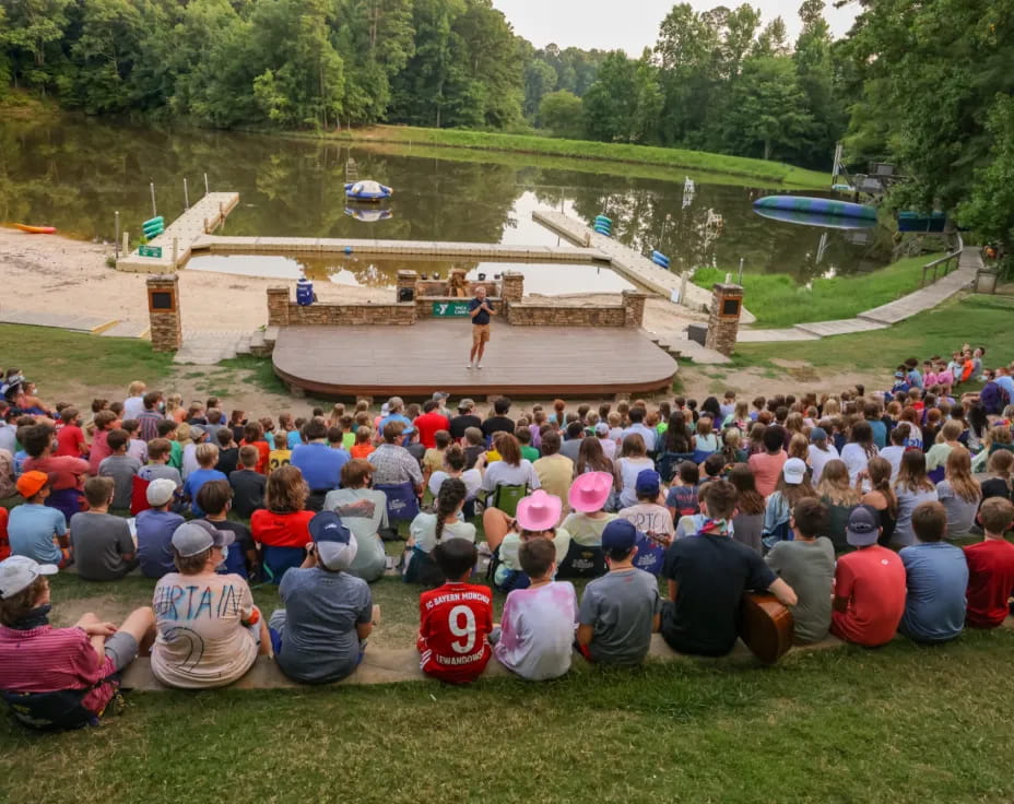 a group of people sitting on the grass looking at a person on a stage