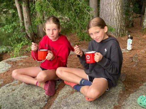 two children sitting on the ground holding cups and eating