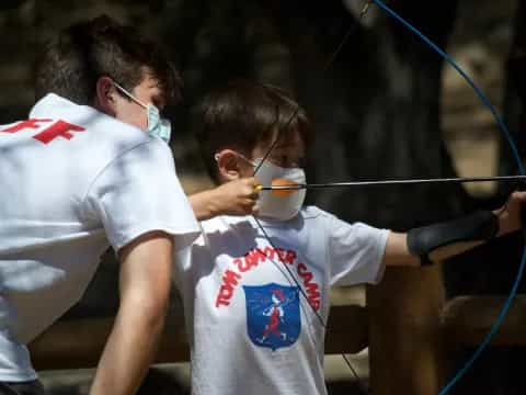 a couple of boys wearing safety goggles and holding a bow and arrow