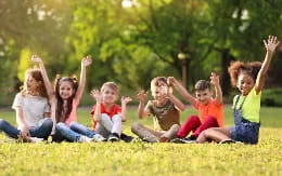 a group of children sitting on the grass with their arms raised