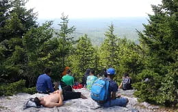 a group of people sitting on a rock overlooking a forest