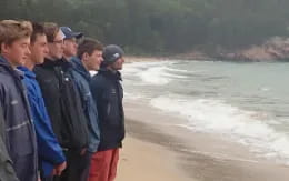 a group of people standing on a beach looking at the water