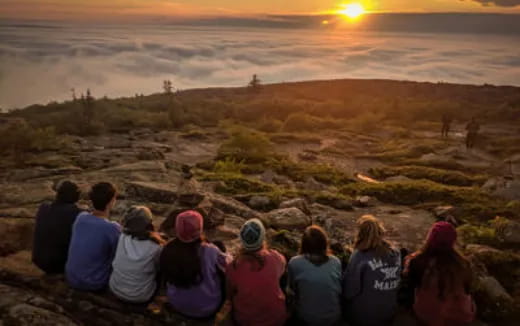 a group of people looking at a landscape with a hill and a sunset