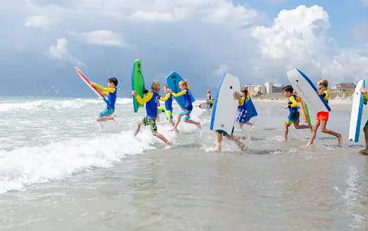 a group of kids carrying surfboards on a beach