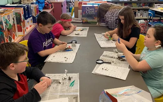 a group of children sitting at a table with paper and pencils