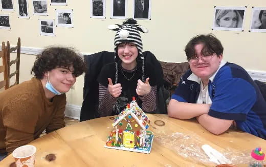 a group of people sitting around a table with a gingerbread house