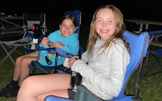 a couple of girls sitting in lawn chairs at night