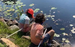 a couple of people sitting on a rock by a body of water