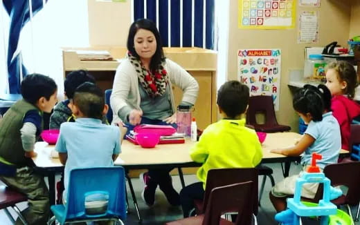 a person standing in front of a group of children sitting at desks