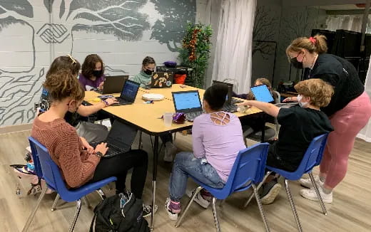 a group of people sitting around a table with laptops