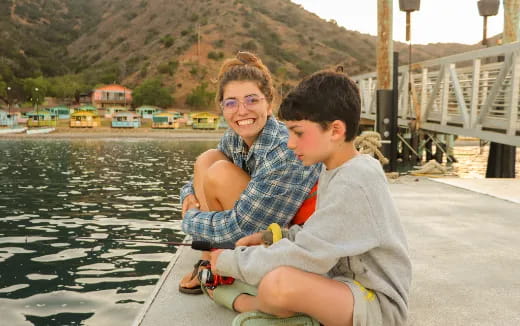 a person and a boy sitting on a dock by a body of water