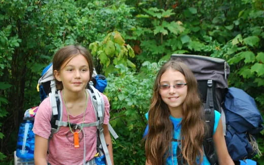 a couple of girls with backpacks in a forest