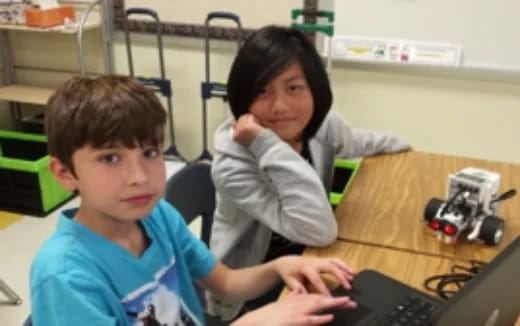 a couple of kids sitting at a table with a computer