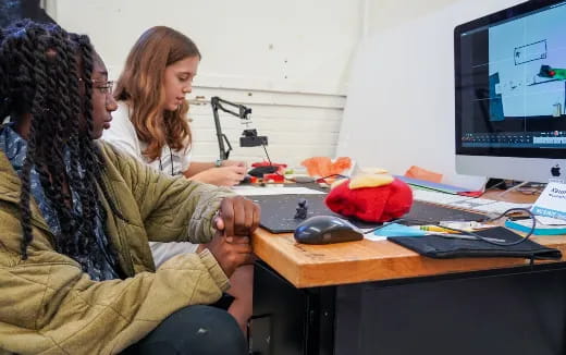 a woman and a man sitting at a desk looking at a computer screen