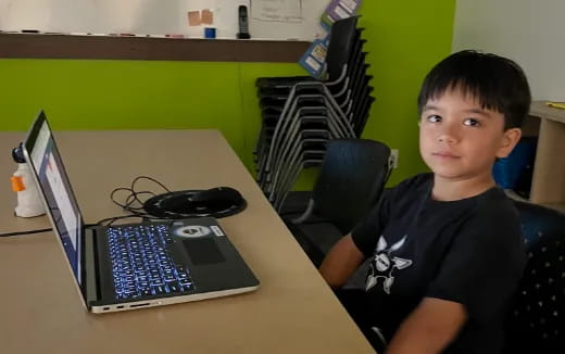 a boy sitting at a desk with a laptop