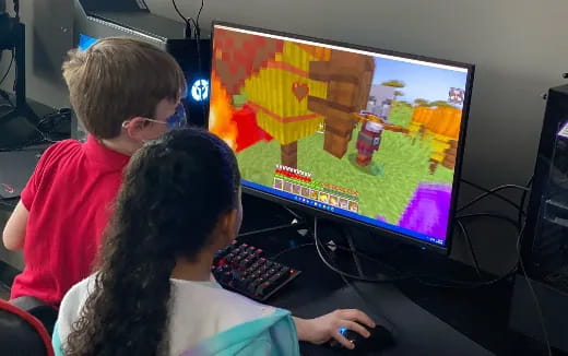 a couple of people sitting at a computer desk looking at a screen