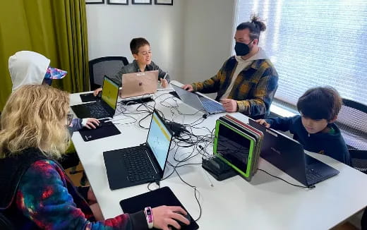 a group of people sitting around a table with laptops