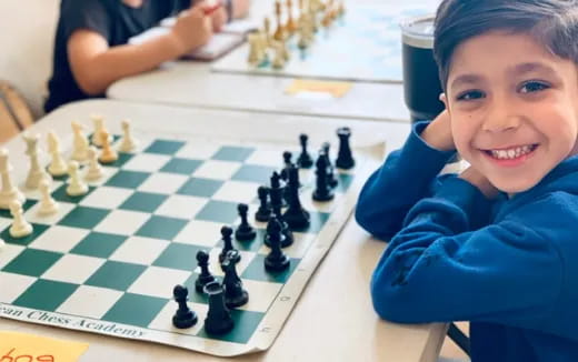 a boy sitting at a table with a chess board and a chess board