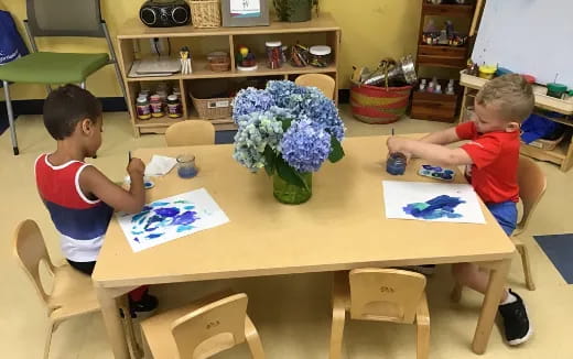 a couple of boys sitting at a table with a vase of flowers