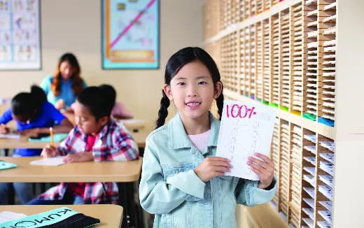 a young girl holding a piece of paper in a classroom