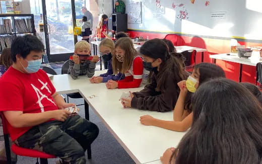 a group of children sitting at a table with a person wearing a mask