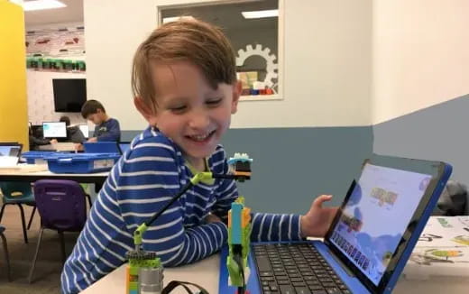 a boy smiling and pointing at a laptop