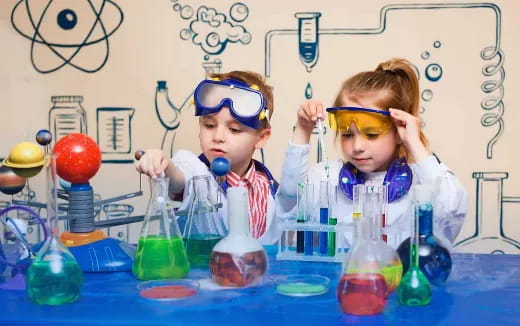 young girls wearing goggles and sitting at a table with vials of liquid