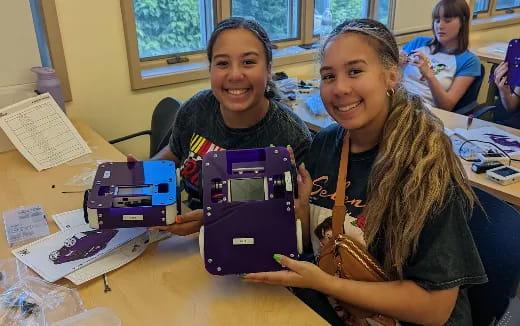 a few girls smiling and sitting at a table with purple and white boxes