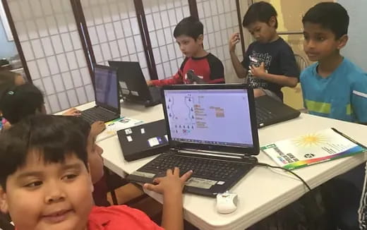 a group of kids sitting at a table with laptops