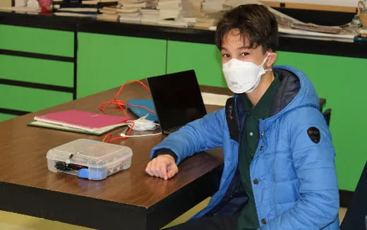 a person wearing a mask and sitting at a desk with a laptop