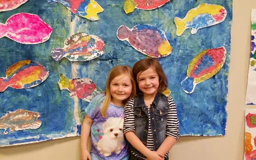 a couple of girls posing for the camera in front of a painting