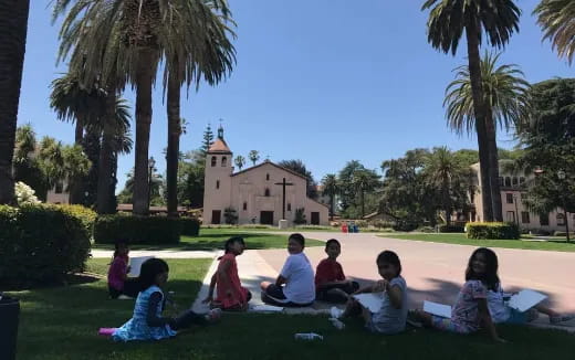 a group of children sitting on the grass in front of a building